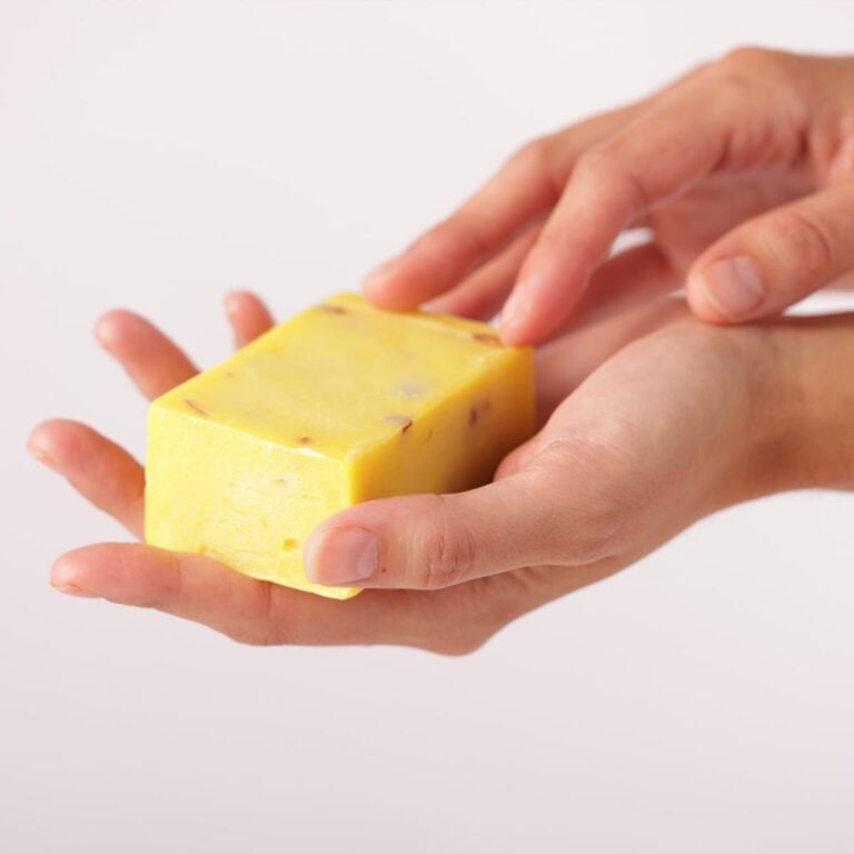Manos sosteniendo una pastilla amarilla de Jabón Natural Caléndula 100g Labnatur con fragmentos vegetales visibles