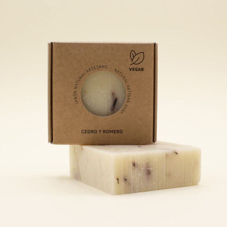 Estuche kraft de Jabón Natural Artesano Cedro y Romero 100g Labnatur apoyado sobre una pastilla crema con fragmentos oscuros