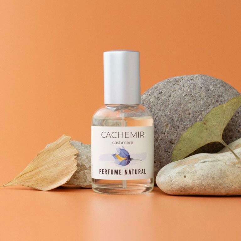 Perfume Cachemir 50ml Labnatur entre piedras naturales y dos hojas secas sobre fondo naranja