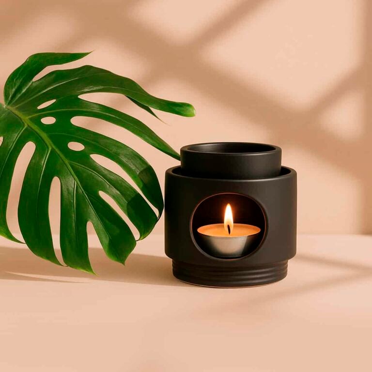 Quemador Noir de cerámica negra SYS Aromas con vela encendida junto a hoja verde de monstera