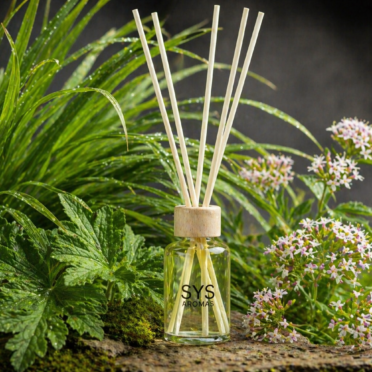 Mikado de citronela SYS Aromas en entorno natural con hojas verdes y flores, con etiqueta decorativa